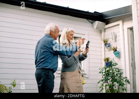 Senior man talking with woman holding mobile phone against house Stock Photo