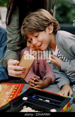 Cropped hand of woman showing mobile phone to children sitting at table Stock Photo