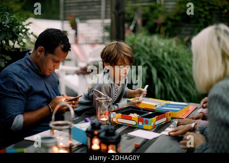 Family playing board game on table while father using mobile phone Stock Photo