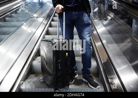 Low section of man with wheeled suitcase standing on escalator Stock Photo