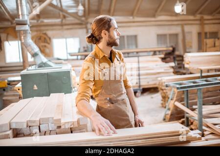 Portrait of a cheerful carpenter standing near the raw wood materials at the carpentry shop warehouse Stock Photo