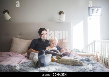 Father reading picture book with toddler son while sitting on bed at home Stock Photo