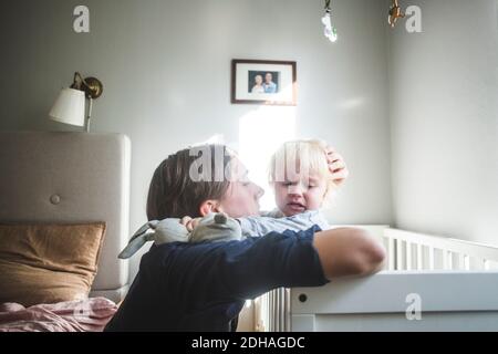 Father consoling crying blond baby boy in crib with tender love at home Stock Photo