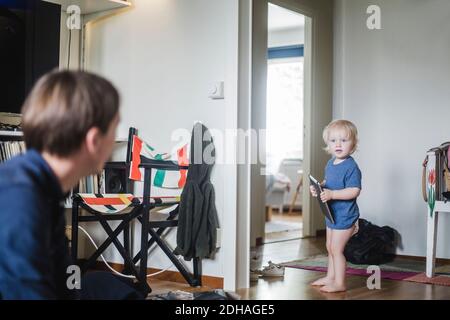 Full length of baby boy holding digital tablet while looking at father in living room Stock Photo