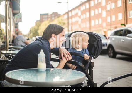 Father and son looking away while sitting at sidewalk cafe in city Stock Photo