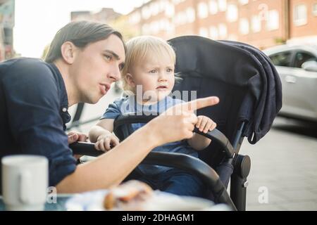 Father pointing while looking away with son at sidewalk cafe in city Stock Photo