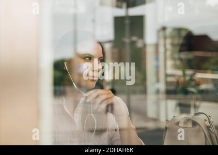 Thoughtful businesswoman wearing headphones seen through glass window at office Stock Photo