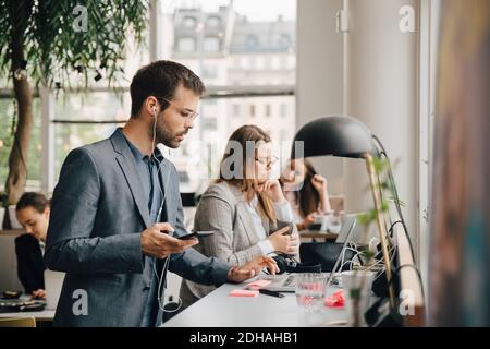 Male professional using laptop and smart phone while working with colleagues at coworking space Stock Photo