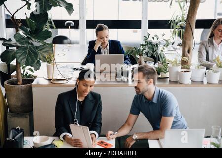 Colleagues discussing while businesswoman working on laptop at office Stock Photo