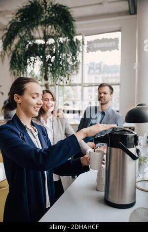 Smiling colleagues looking at businesswoman having coffee during break Stock Photo