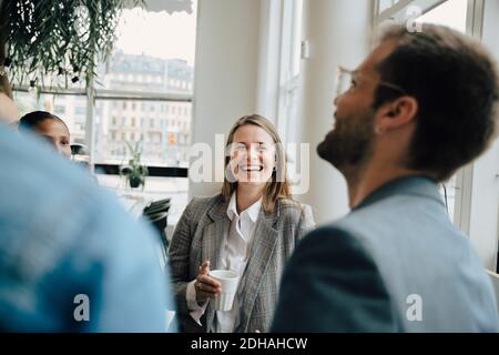 Smiling businesswoman having coffee with colleagues at creative workplace Stock Photo