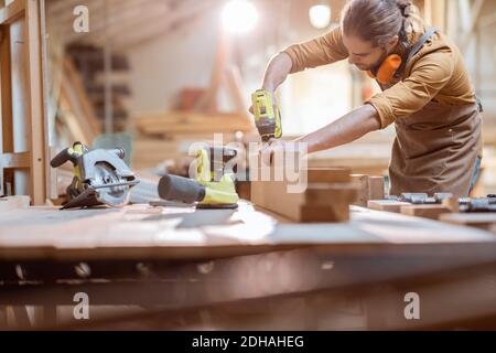 Carpenter working with modern cordless tools and wooden bars on the workbench at the workshop Stock Photo