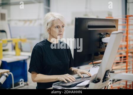 Serious mature woman using computer while standing in industry Stock Photo