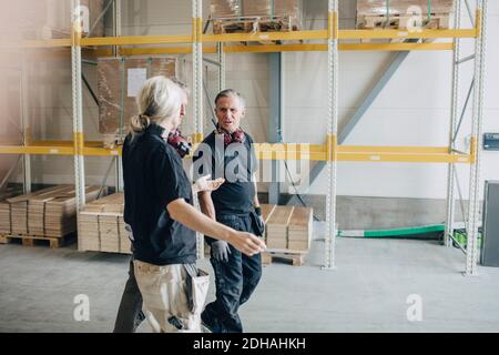 Confident male and female workers talking while walking by rack in lumber industry Stock Photo