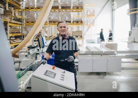 Portrait of smiling senior worker standing by machine at industry Stock Photo