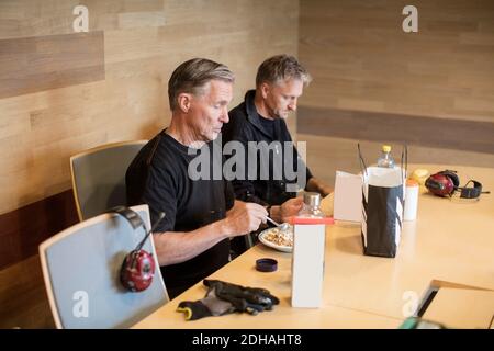 Workers having lunch at table while sitting against wall in industry Stock Photo