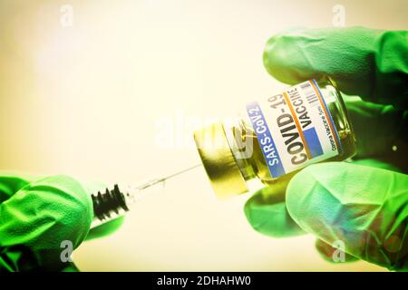 Hände in Schutzhandschuhen halten Injektionsfläschchen mit Corona-Impfstoff und Impfspritze, Symbolfoto Corona-Impfmittel