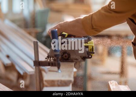 Carpenter sawing wooden bars with cordless electric saw at the joiner's workshop. Close-up with no face Stock Photo