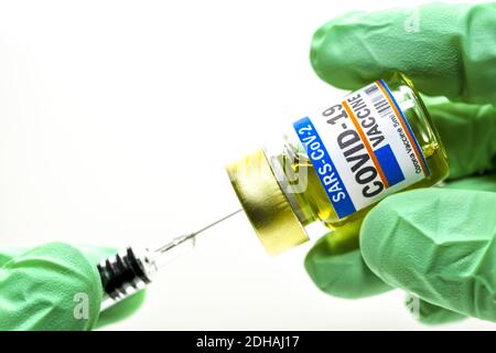 Hände in Schutzhandschuhen halten Injektionsfläschchen mit Corona-Impfstoff und Impfspritze, Symbolfoto Corona-Impfmittel