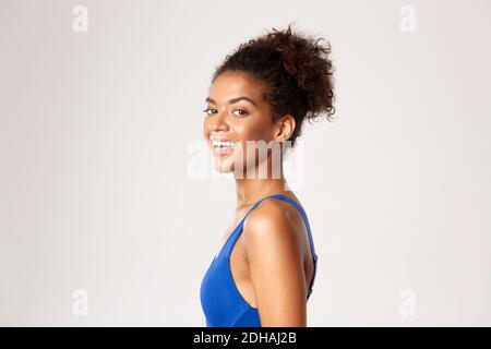 Concept of workout and sport. Close-up profile shot of happy, athletic woman in blue fitness clothing, turn head at camera and l Stock Photo