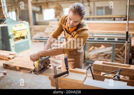 Carpenter sawing wooden bars with cordless electric saw at the joiner's workshop Stock Photo