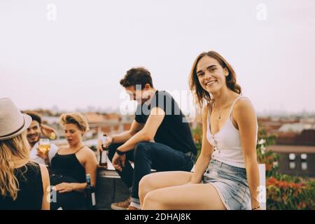Smiling young woman sitting with friends at rooftop party Stock Photo