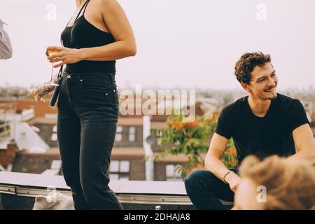 Woman with beer standing by friend looking away on terrace at party Stock Photo