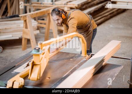 Carpentry worker sawing wooden planks with circular saw in the joinery warehouse Stock Photo