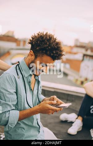 Smiling young man text messaging on smart phone at terrace party Stock Photo