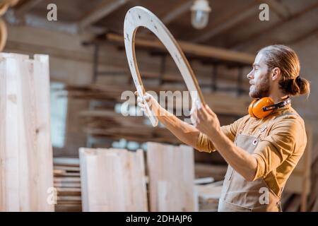 Portrait of a handsome carpenter looking on the wooden product, constructing goods with plywood at the workshop Stock Photo