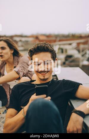 Young man using smart phone while friend enjoying at rooftop party Stock Photo