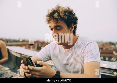 Young man text messaging through smart phone while sitting on terrace in city Stock Photo