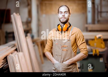 Portrait of a handsome carpenter in uniform and headphones at the workshop Stock Photo