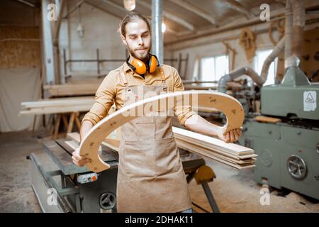 Portrait of a handsome carpenter looking on the wooden product, constructing goods with plywood at the workshop Stock Photo