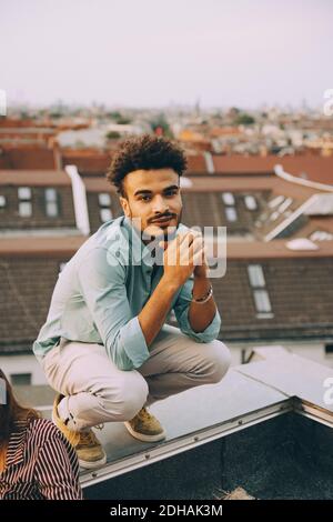 Portrait of young man with hands clasped crouching on retaining wall at terrace Stock Photo