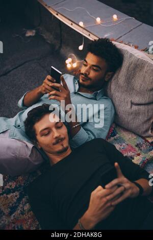 High angle view of male friends using smart phones while lying on terrace at dusk Stock Photo