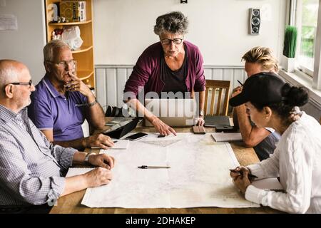 Female instructor explaining senior men and woman over map at table during navigation course Stock Photo