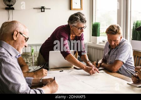 Female instructor explaining senior men over map at table during navigation course Stock Photo