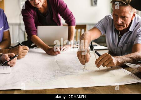 Female instructor guiding senior men using drawing compass on map at table during navigation course Stock Photo