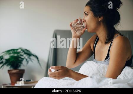 Woman taking medicine while sitting on bed at home Stock Photo