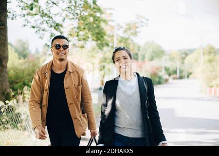Portrait of smiling friends talking while walking on street in city during sunny day Stock Photo