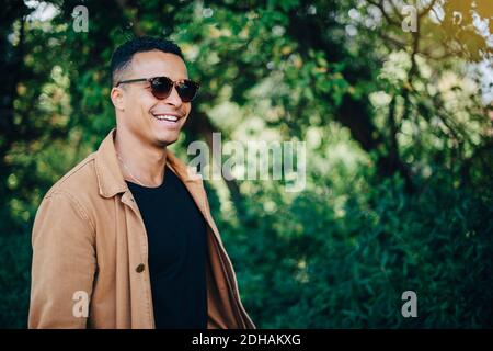 Close-up of smiling man wearing brown jacket standing by plants Stock Photo