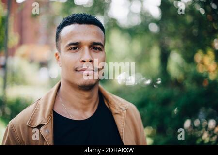 Close-up portrait of man wearing brown jacket standing by plant Stock Photo