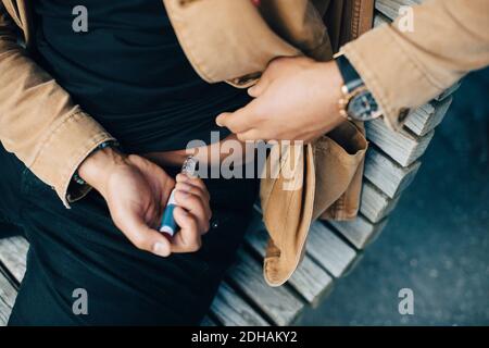 Midsection of man injecting insulin while sitting on bench Stock Photo