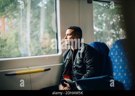 Thoughtful man looking through window while sitting in train Stock Photo