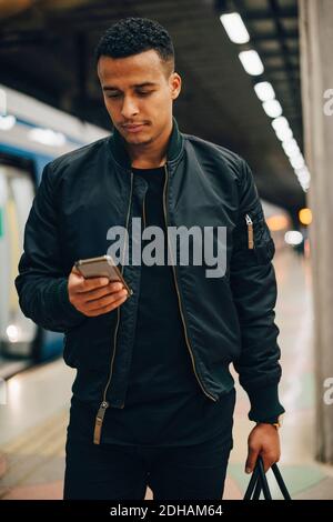 Man using mobile phone while standing by train at subway station Stock Photo