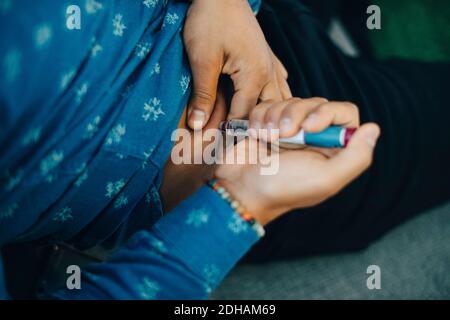 Midsection of businessman injecting insulin in abdomen while sitting on sofa Stock Photo