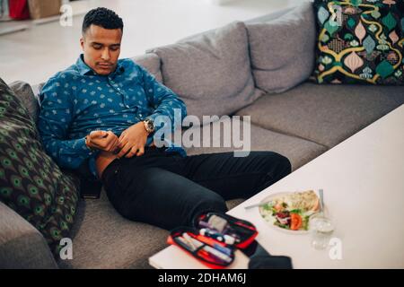 Businessman injecting insulin in abdomen while sitting on sofa in office Stock Photo