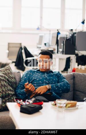 Businessman injecting insulin while sitting on sofa in office Stock Photo