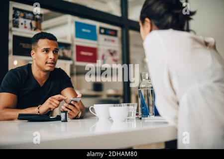Businessman talking to colleague and using mobile phone while doing blood sugar test while sitting at table in office Stock Photo